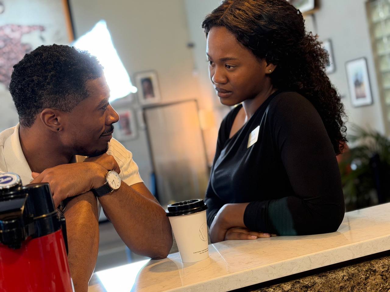 Jordan and Maya talking across the coffee shop counter in Between Two Lives